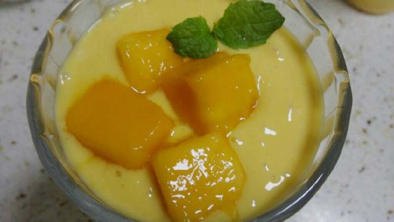 芒果酸奶昔,放入几块切好的芒果果肉，用一根薄荷叶作装饰。
