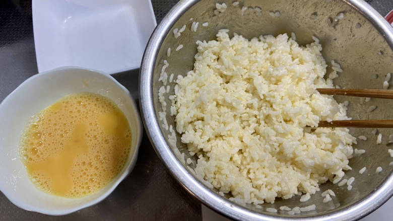 玉米虾仁蛋炒饭,两个鸡蛋打散搅拌均匀，一个鸡蛋打入剩米饭，戴上手套把米饭捏散，蛋液和米饭抓拌均匀