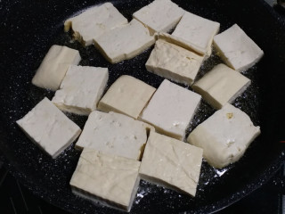 孜然煎豆干,锅中倒入油，油烧热以后，把豆腐一片一片放进锅中煎。