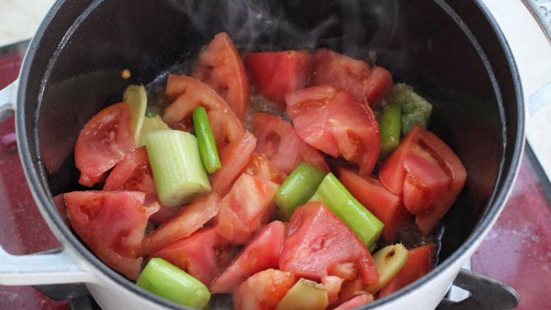 番茄排骨煲,锅中加入一大勺食用油烧热，先放葱段和姜片炒出香味，再把一半的番茄块放进去炒出汤汁。