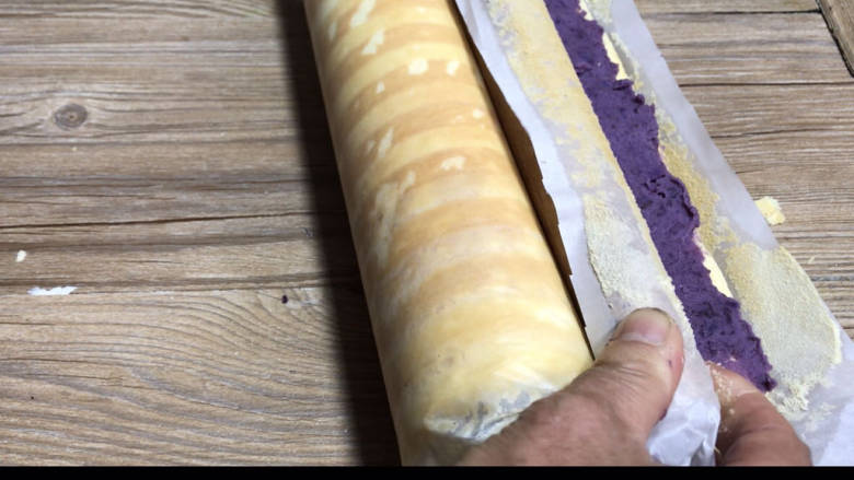 紫薯蛋糕卷,借用擀面杖卷起油纸，将蛋糕推压卷成卷，静置片刻定型