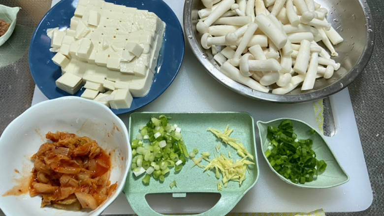 海鲜菇豆腐汤,绢豆腐去包装切小块，海鲜菇去根部清洗切段，小葱切末，葱白葱叶分开，姜切丝，泡菜切小段