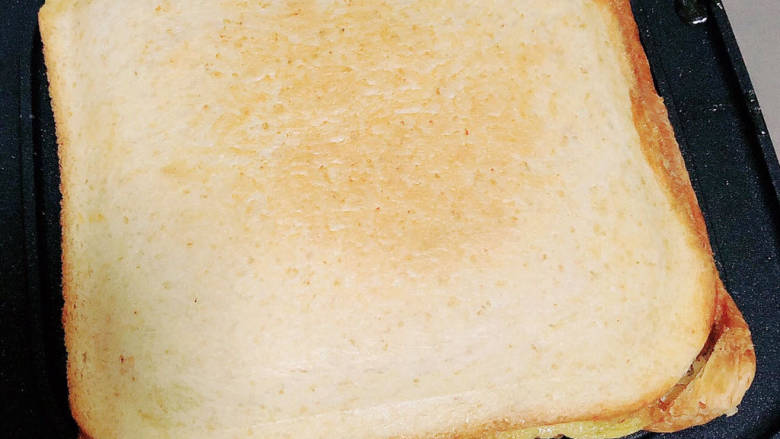 爆浆吐司,再盖上一片切片面包，盖上煎锅的盖子，小火煎2-3分钟。芝士碎融化，即可开盖儿，三明治就做好了。
